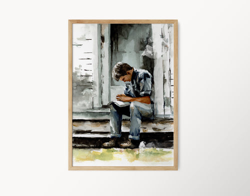 watercolor painting of a young man praying on a porch with open scriptures across his lap he is sitting in front of a white house with gray shadows on the house and front door painting is in a light wood frame frame is against a plain white background
