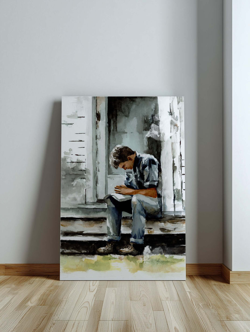 watercolor painting of a young man praying on a porch with scriptures open across his lap painting is large and leaning against a gray wall and sitting on the floor of a light colored hardwood floor