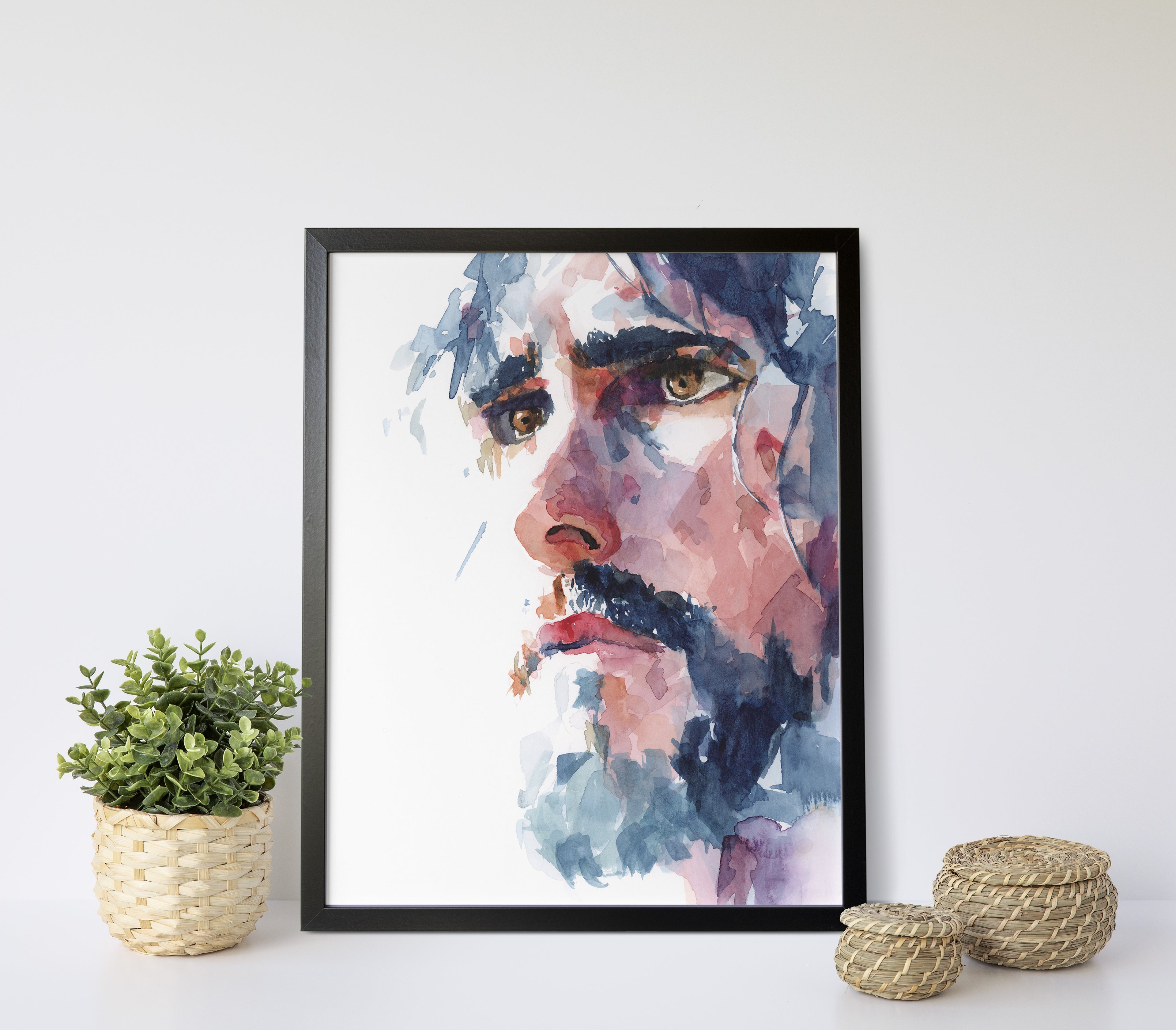 Watercolor portrait painting of Christ looking off into the distance with a serious yet gentle expression dark colored hair falls around his face with dark brows and a dark beard and brown eyes painting is in a black frame against a light background with 